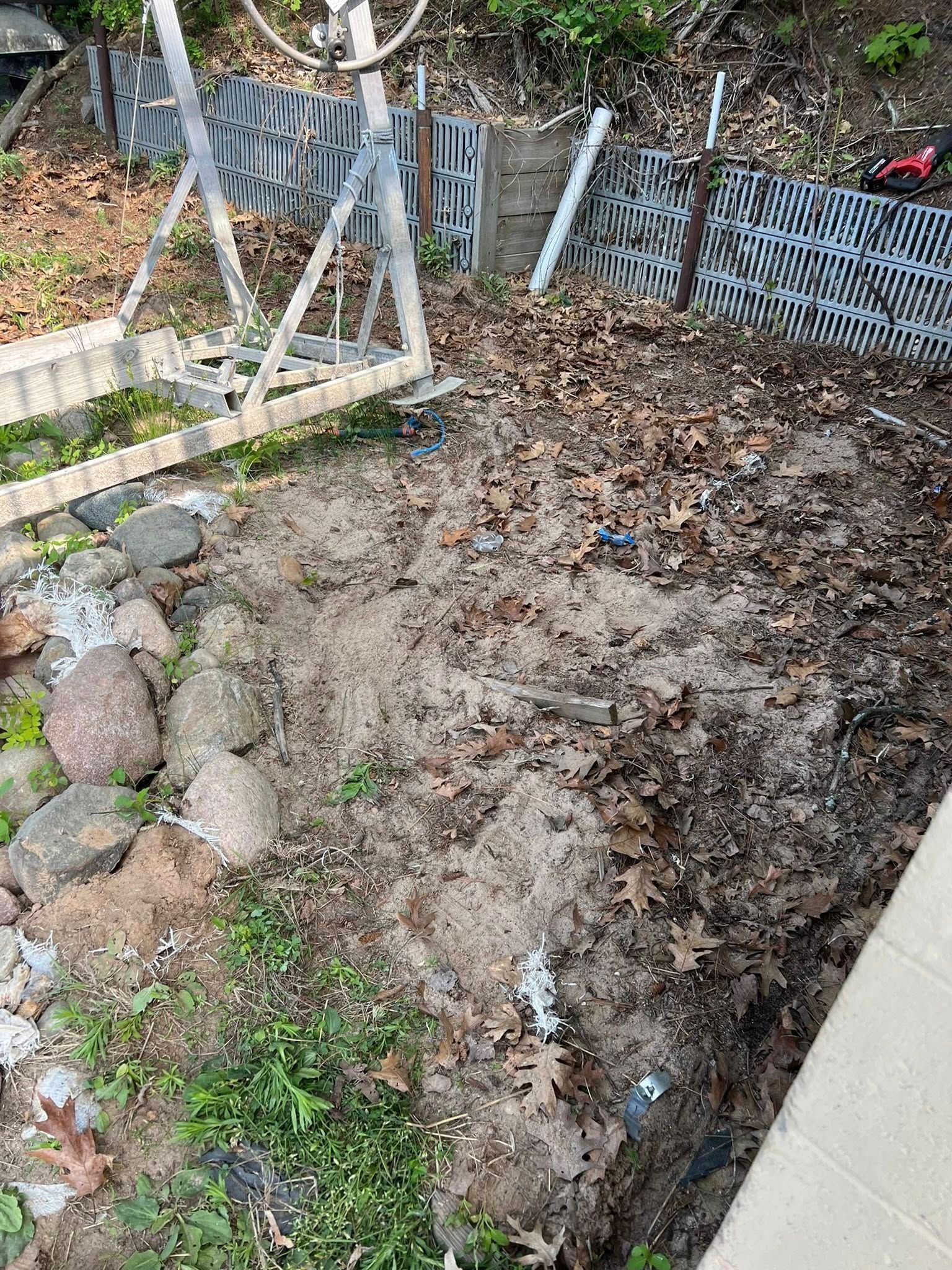 A section of dirt and leaf litter on the ground next to a metal boat lift frame and a gray lattice fence.
