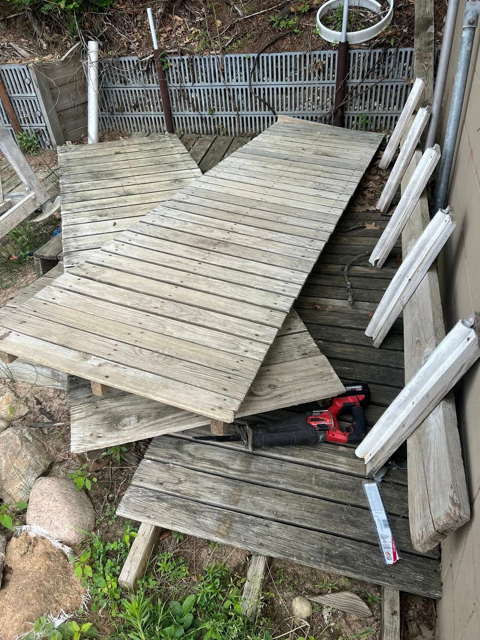 Several perforated metal panels stacked on top of a weathered wooden outdoor platform near a wall.