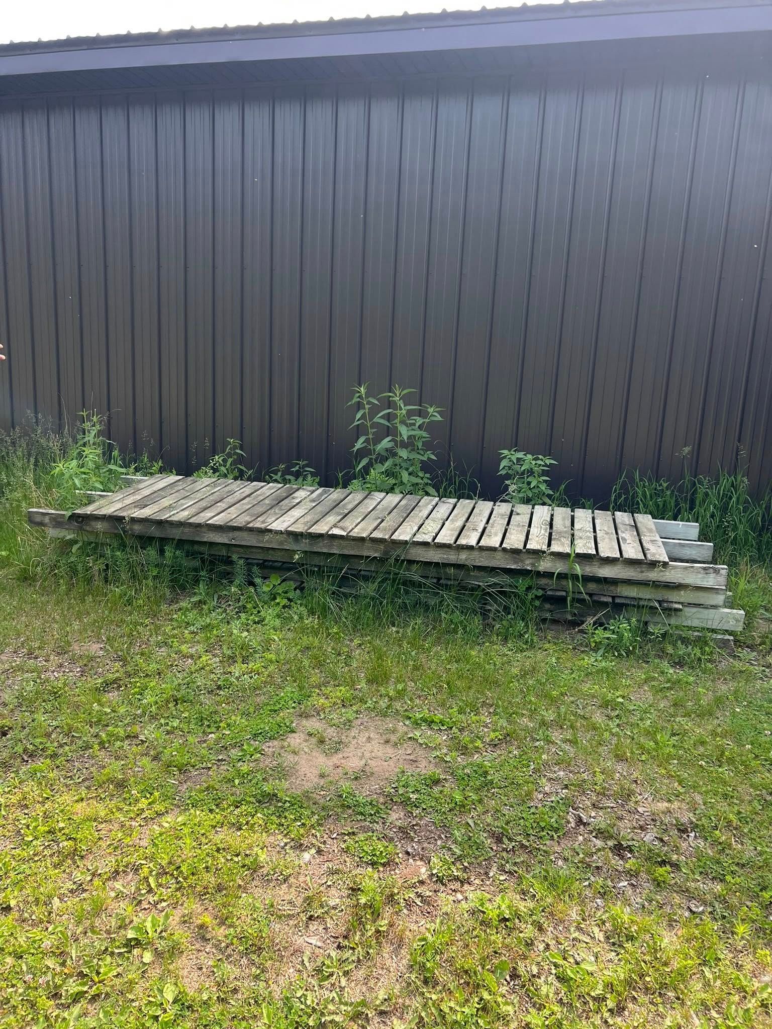 A weathered wooden pallet stack sits in the grass against the dark brown metal siding of a building.