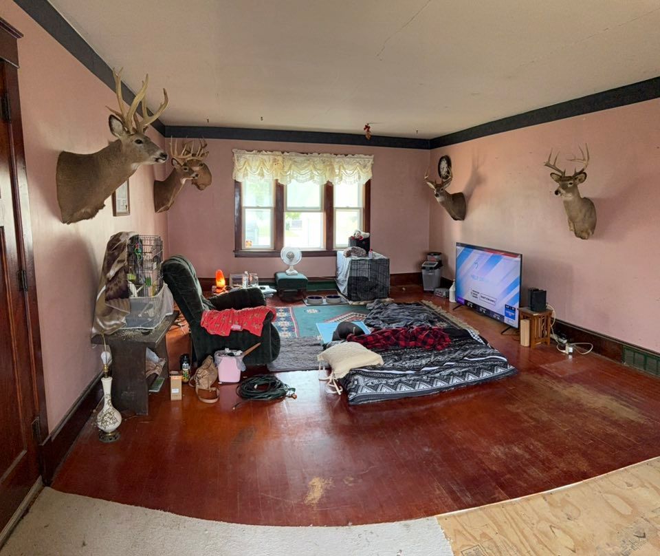 A living room with pink walls, dark wood trim, deer mounts on the walls, a recliner, a floor mattress, and a television.