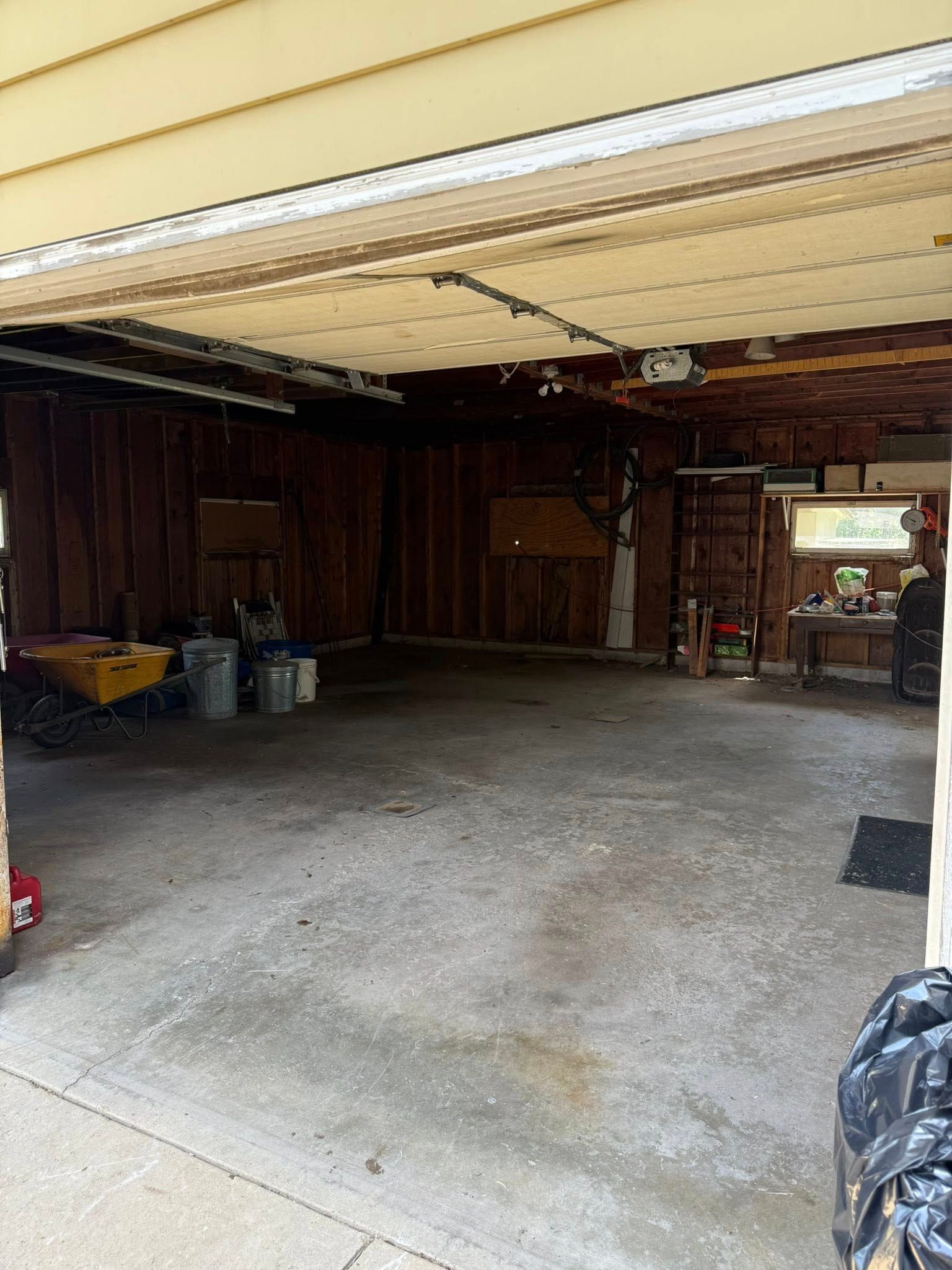 An open, empty, two-car garage with unfinished wooden walls, a concrete floor, and some scattered storage items.