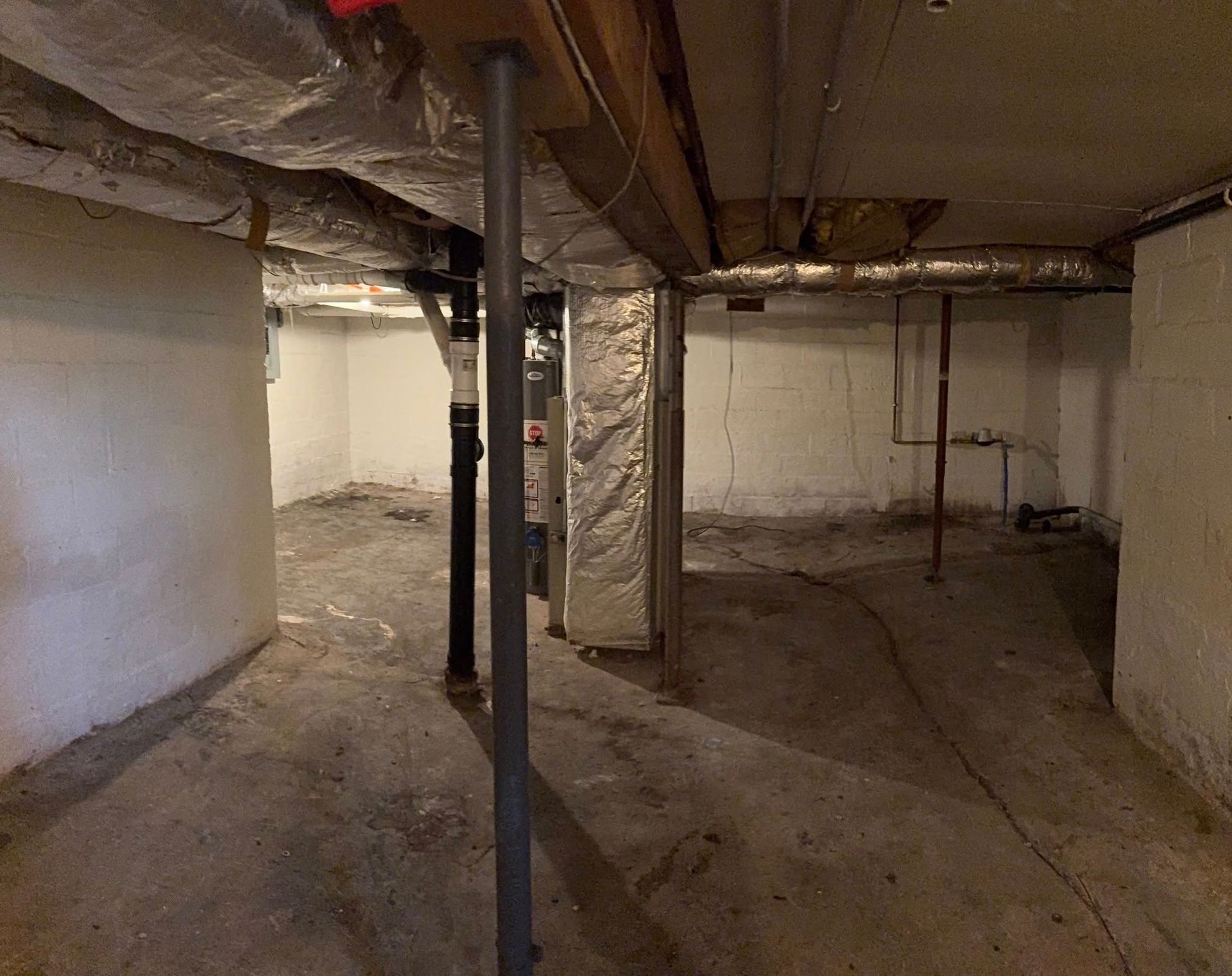 An unfinished basement with a concrete floor, structural steel support poles, exposed ceiling joists, and utility pipes.