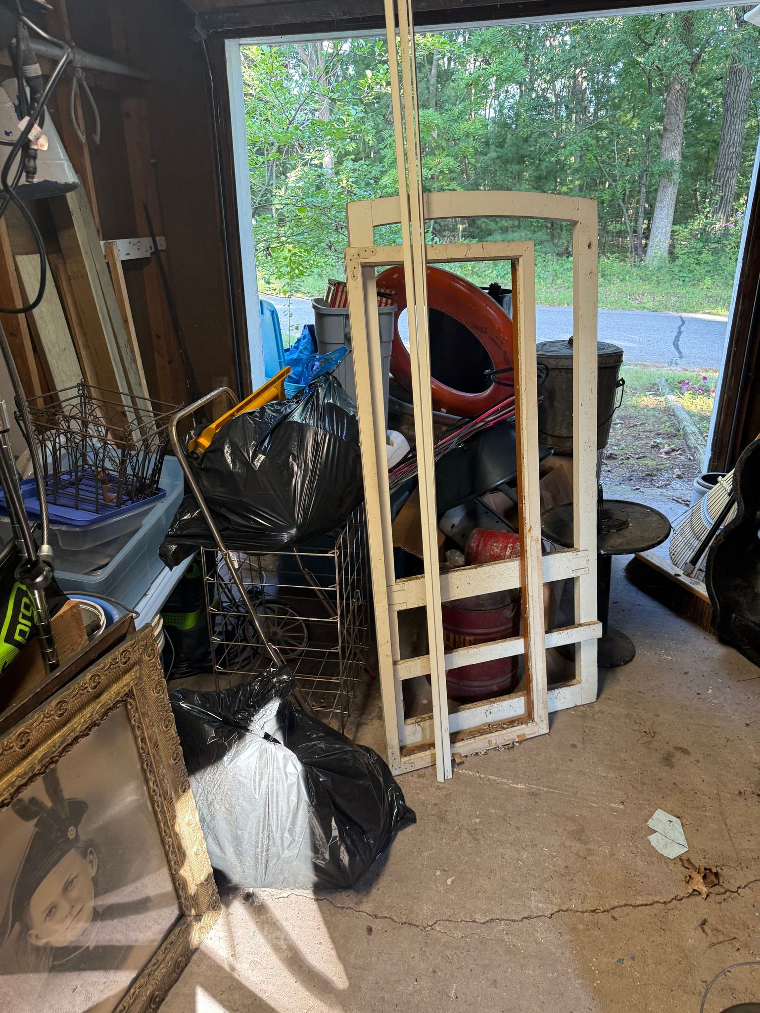 A cluttered garage interior featuring two light-wood frames standing upright, plastic trash bags, and various objects.