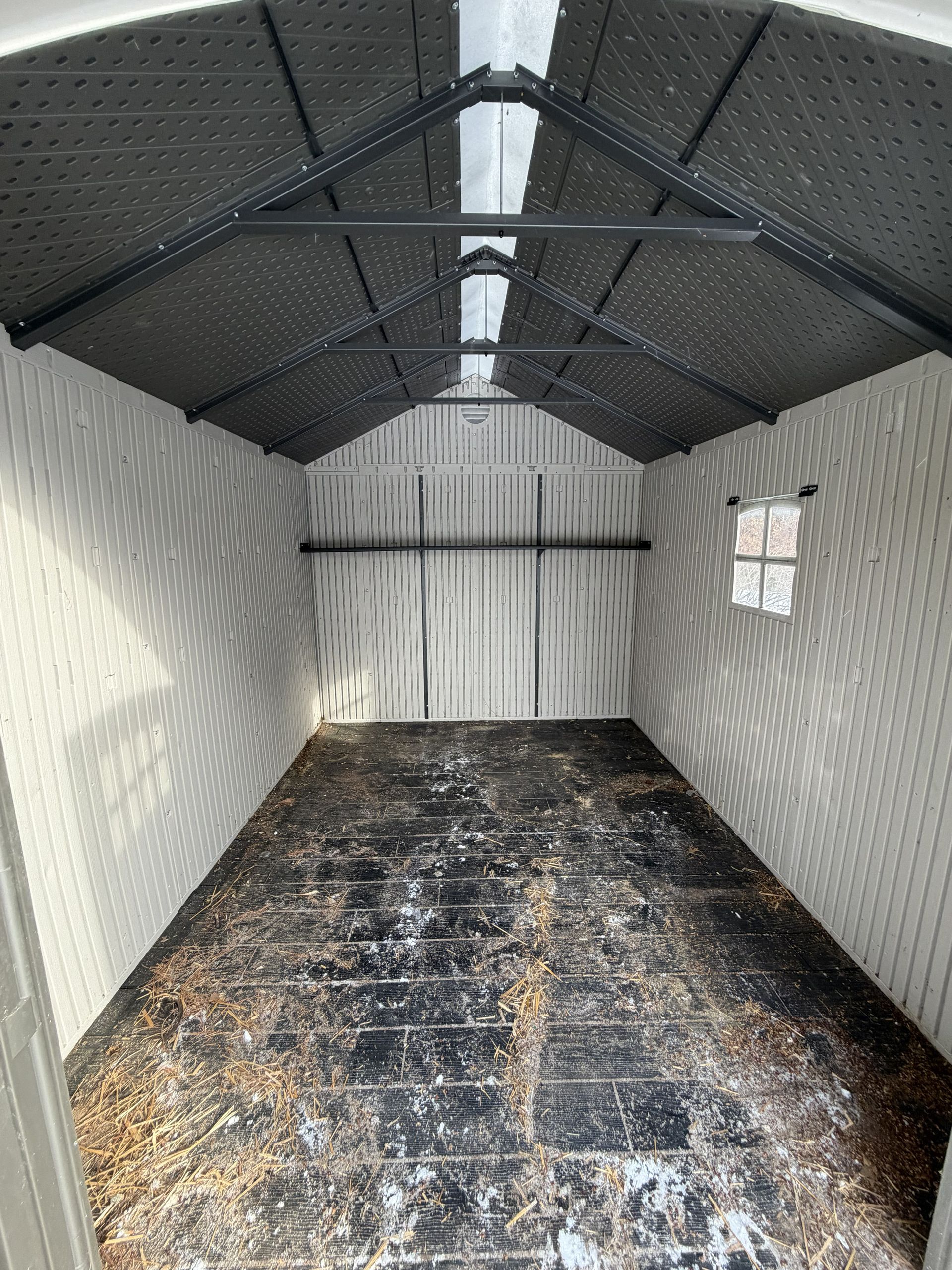 Interior of an empty, light-colored resin shed with a dark roof and floor, and a small window on the right wall.