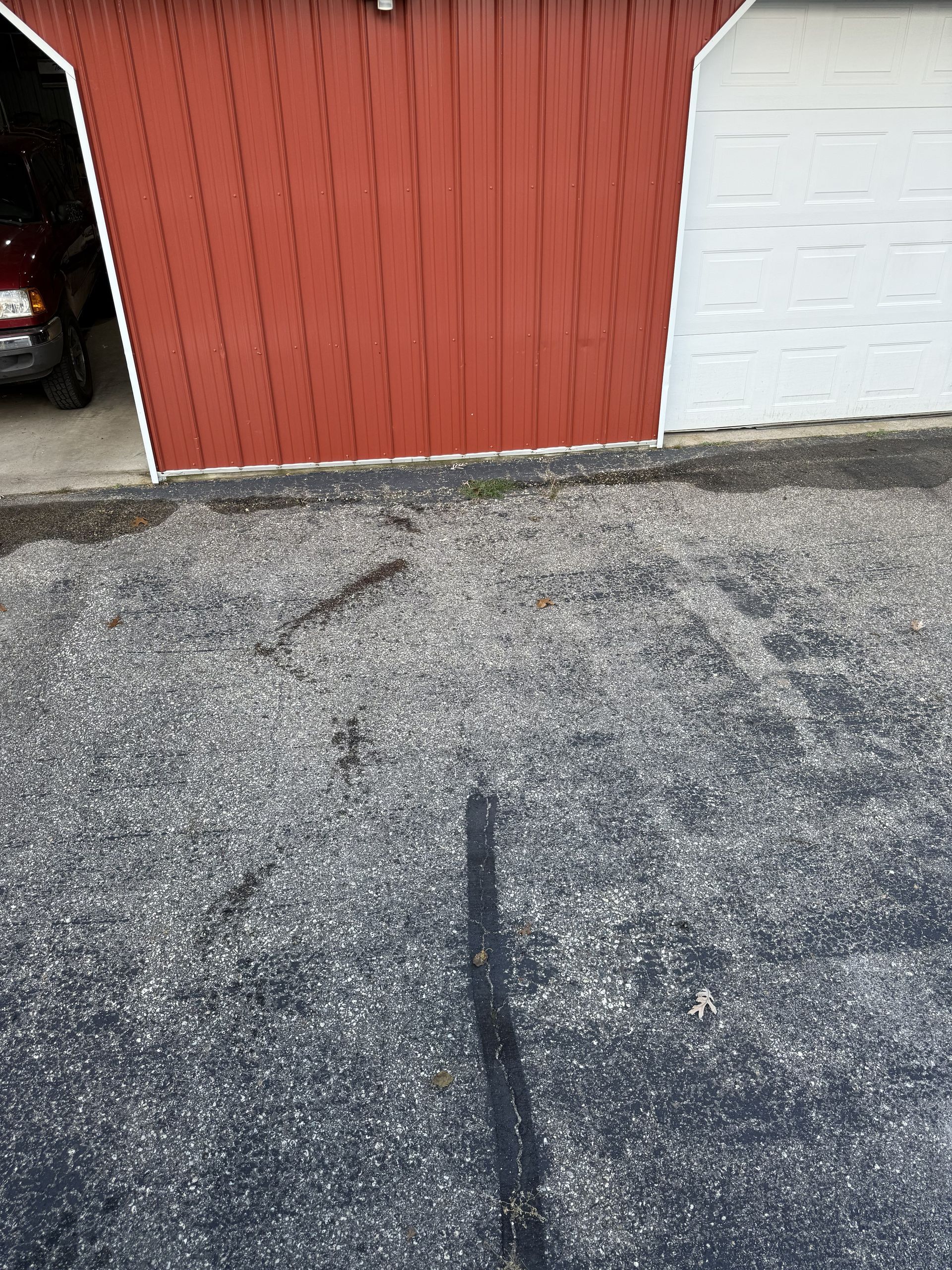 A red and white garage structure seen from a gravel driveway, with a small portion of a dark vehicle visible on the left.