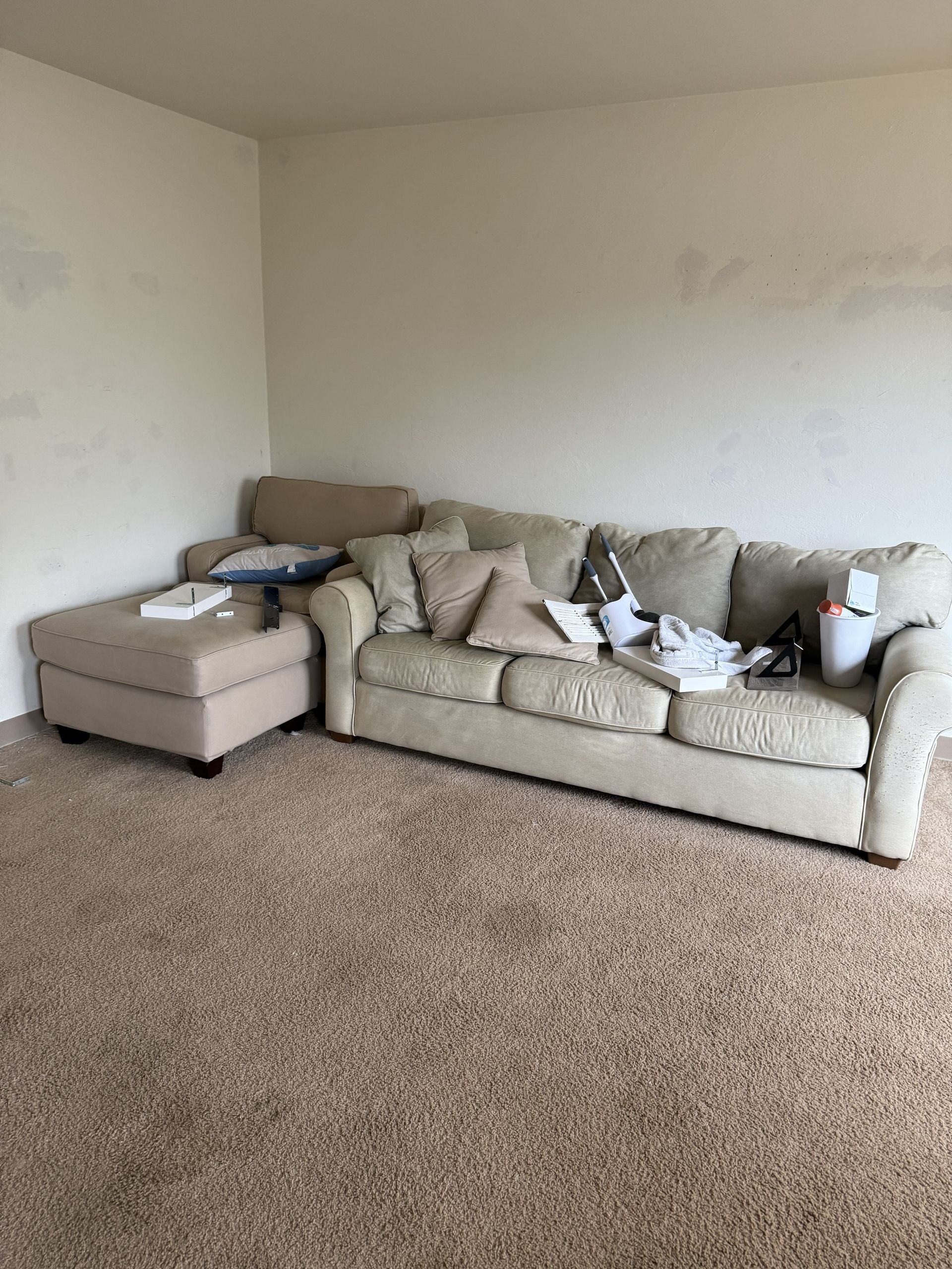 A beige sectional sofa sits in a room with light-colored walls and tan carpet.