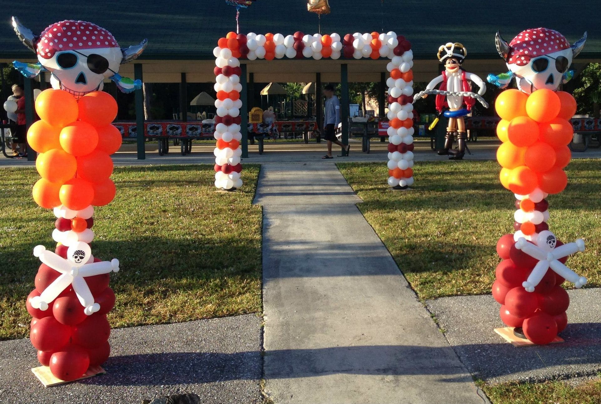 Two pirate-themed balloon columns with skull toppers stand on either side of a path leading to a balloon-arched pavilion.