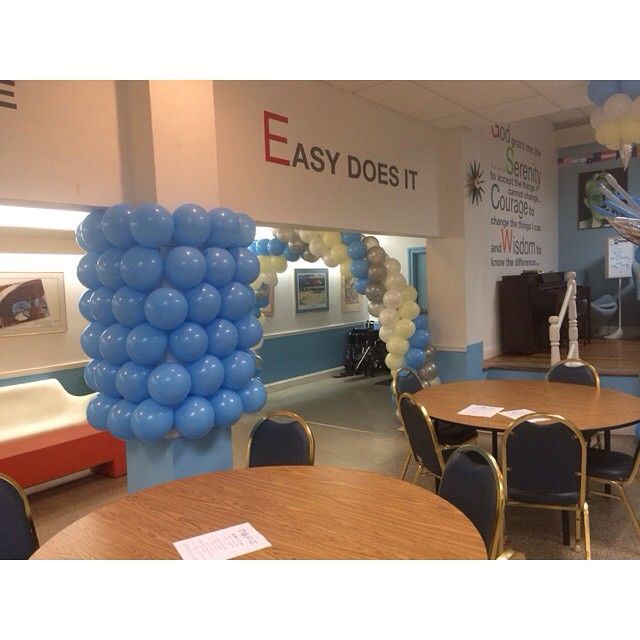 A room decorated with blue and white balloons, featuring a pillar covered in blue balloons and a large balloon archway.