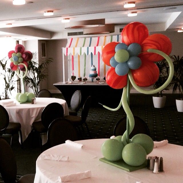 Large balloon flowers in red and blue with green stems serve as table centerpieces in a decorated event hall.