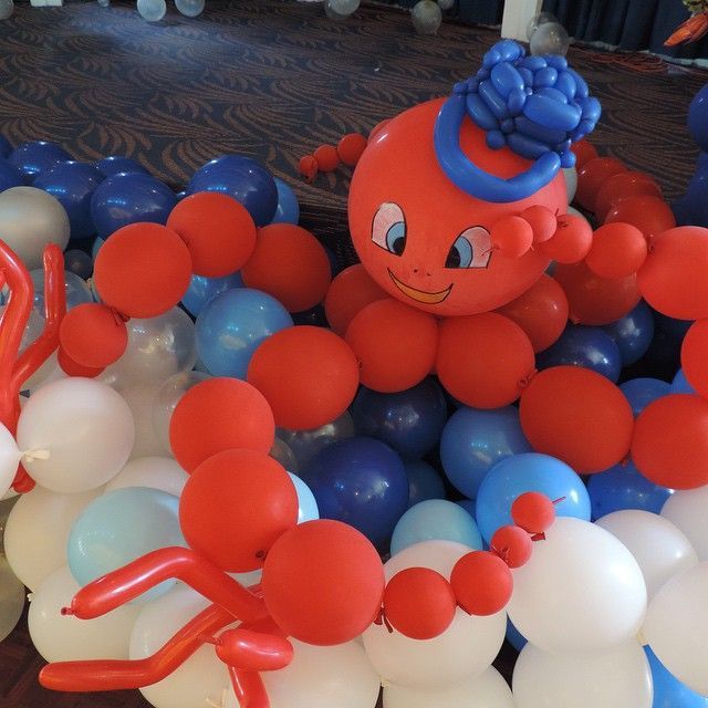 An octopus decoration made of red, blue, and white balloons, featuring a cartoon face with a blue bow atop its head.