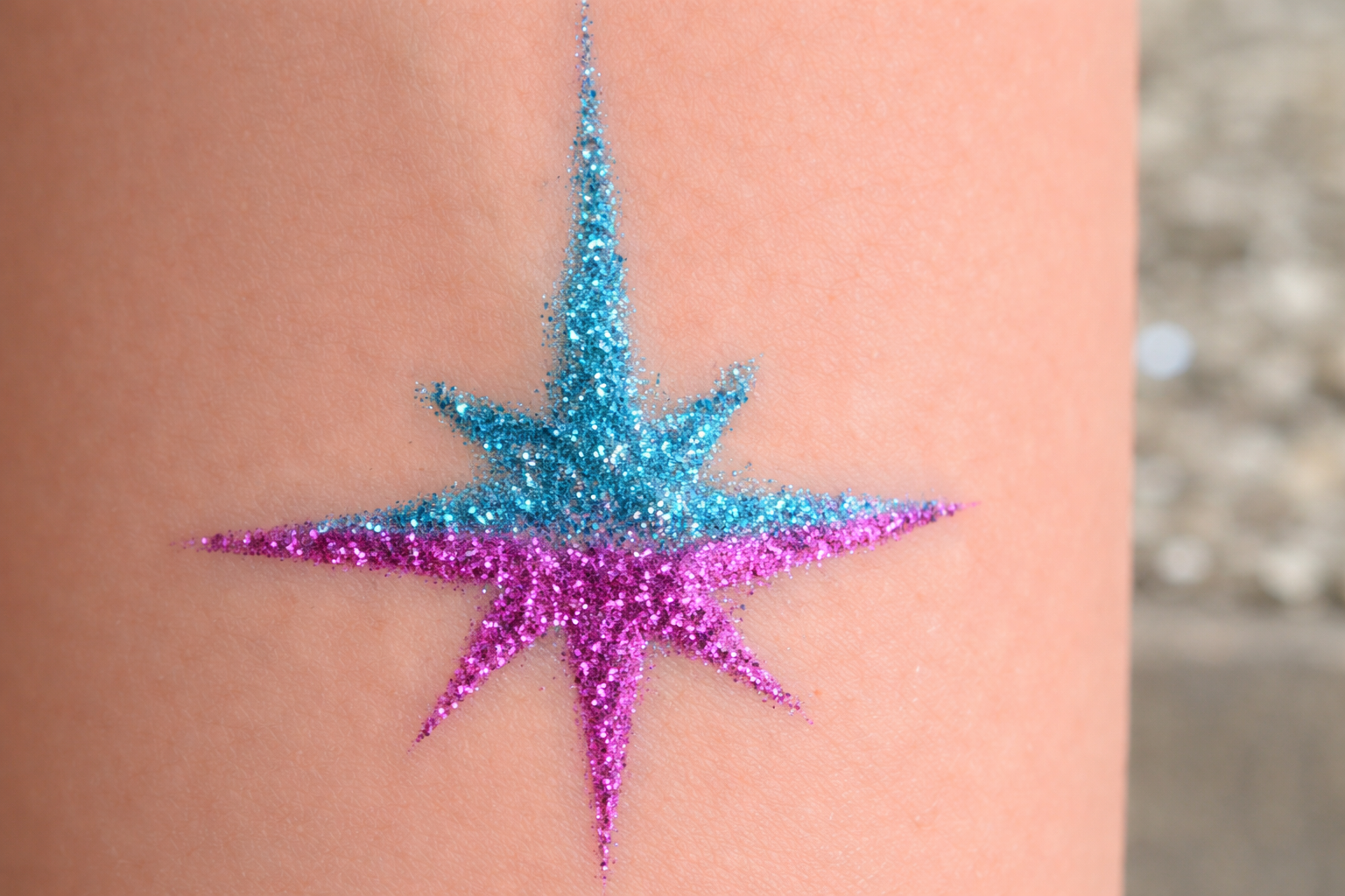 A glittery eight-pointed star tattoo on skin, with the top half in blue and the bottom half in purple.