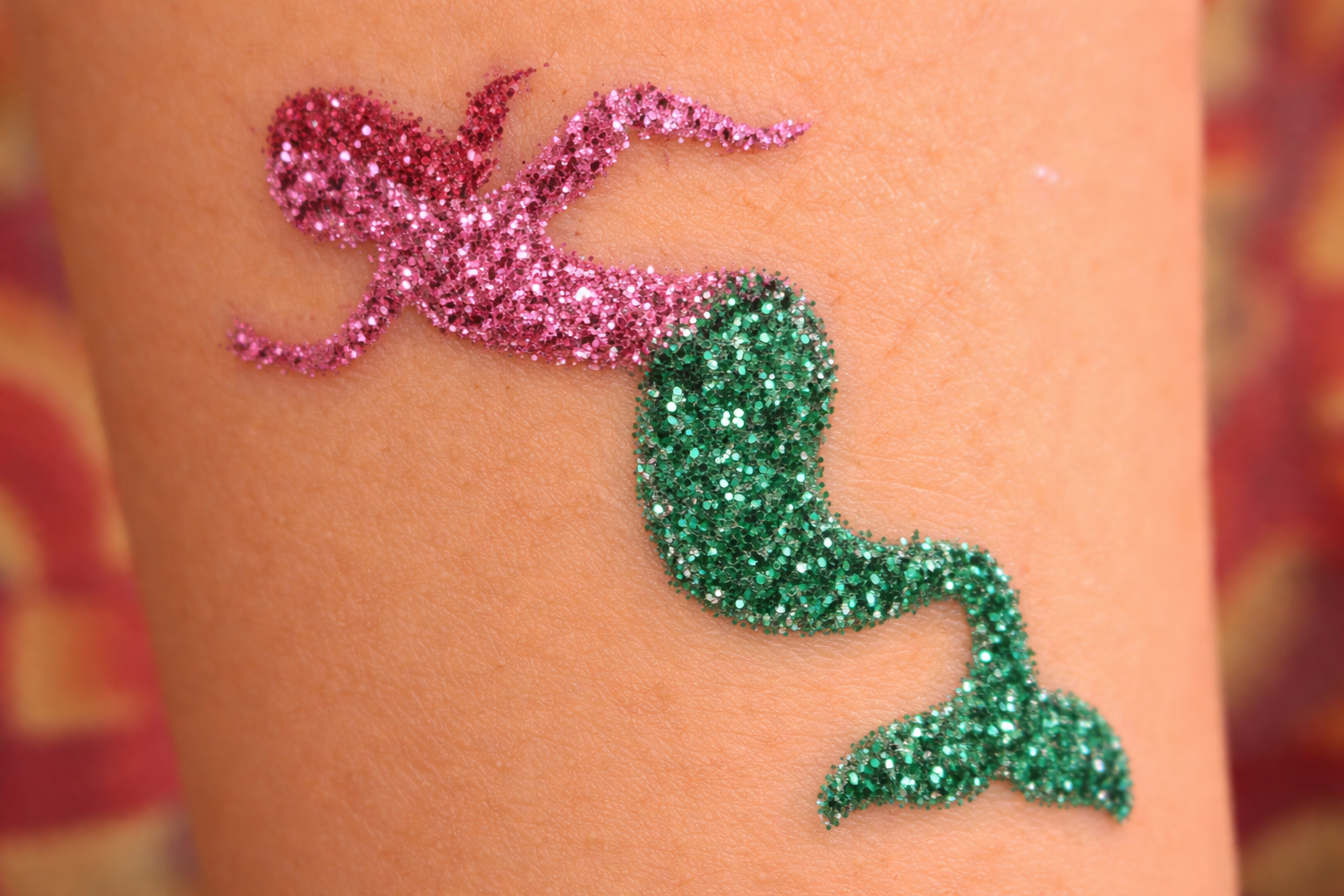 A glitter tattoo of a mermaid with a pink upper body and a green, sparkly tail on a person's skin.