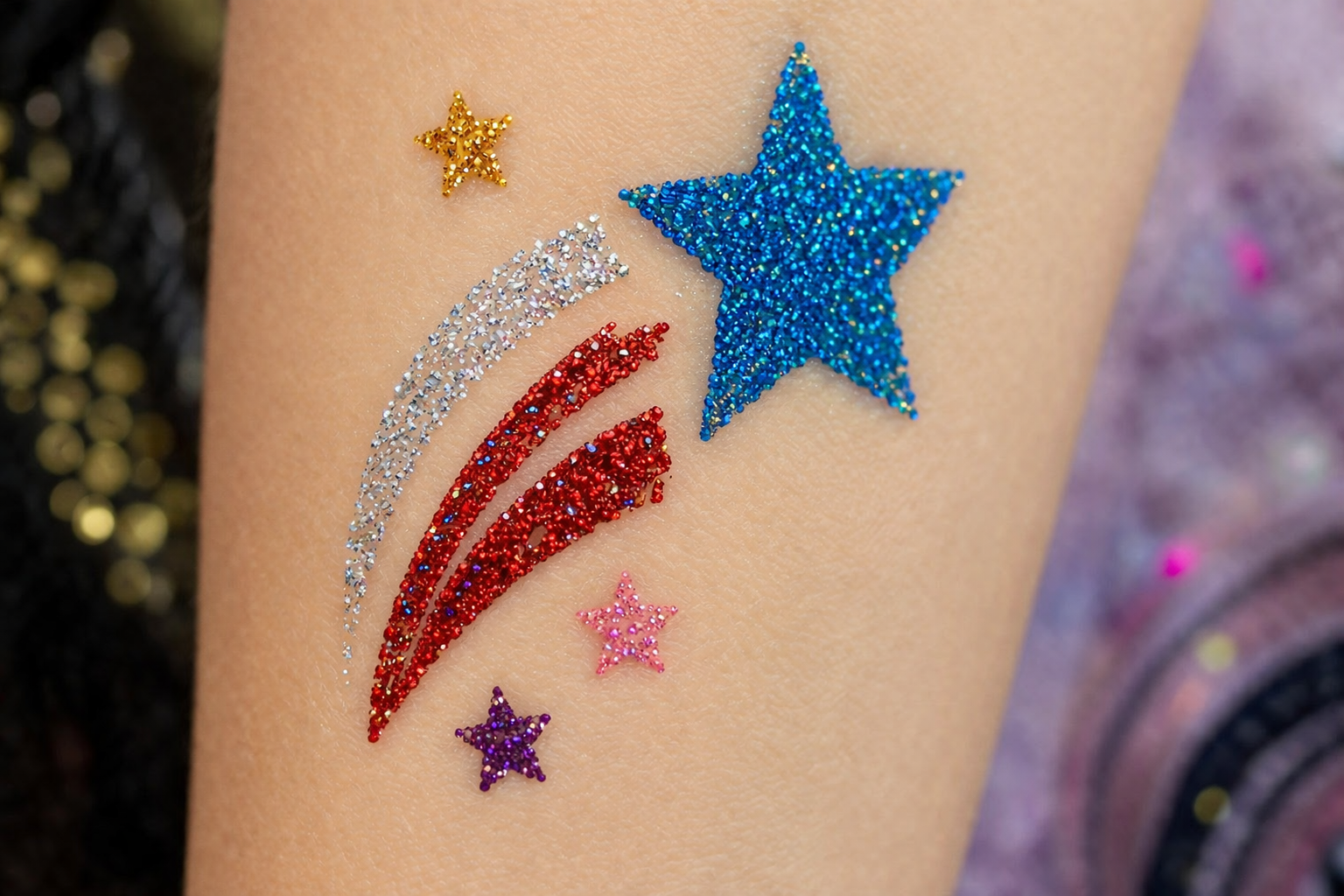A glittery tattoo on skin featuring a large blue star, silver and red swooshes, and small gold, pink, and purple stars.