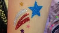 Glitter tattoo on skin featuring a blue star, silver and red swooshes, and several smaller colorful stars.