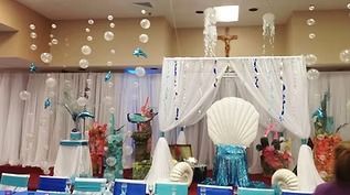 An under-the-sea themed event setup featuring a large seashell chair, white drapes, and hanging bubble decorations.