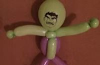 A balloon animal of the Hulk with a green head, green arms, and a purple body on a reddish background.