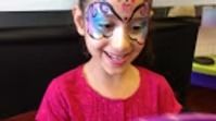 A smiling person wearing a colorful, detailed butterfly face paint design across their eyes and forehead.