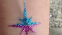 A glittery, eight-pointed star tattoo on skin, featuring a bright blue top half and a vibrant purple bottom half.