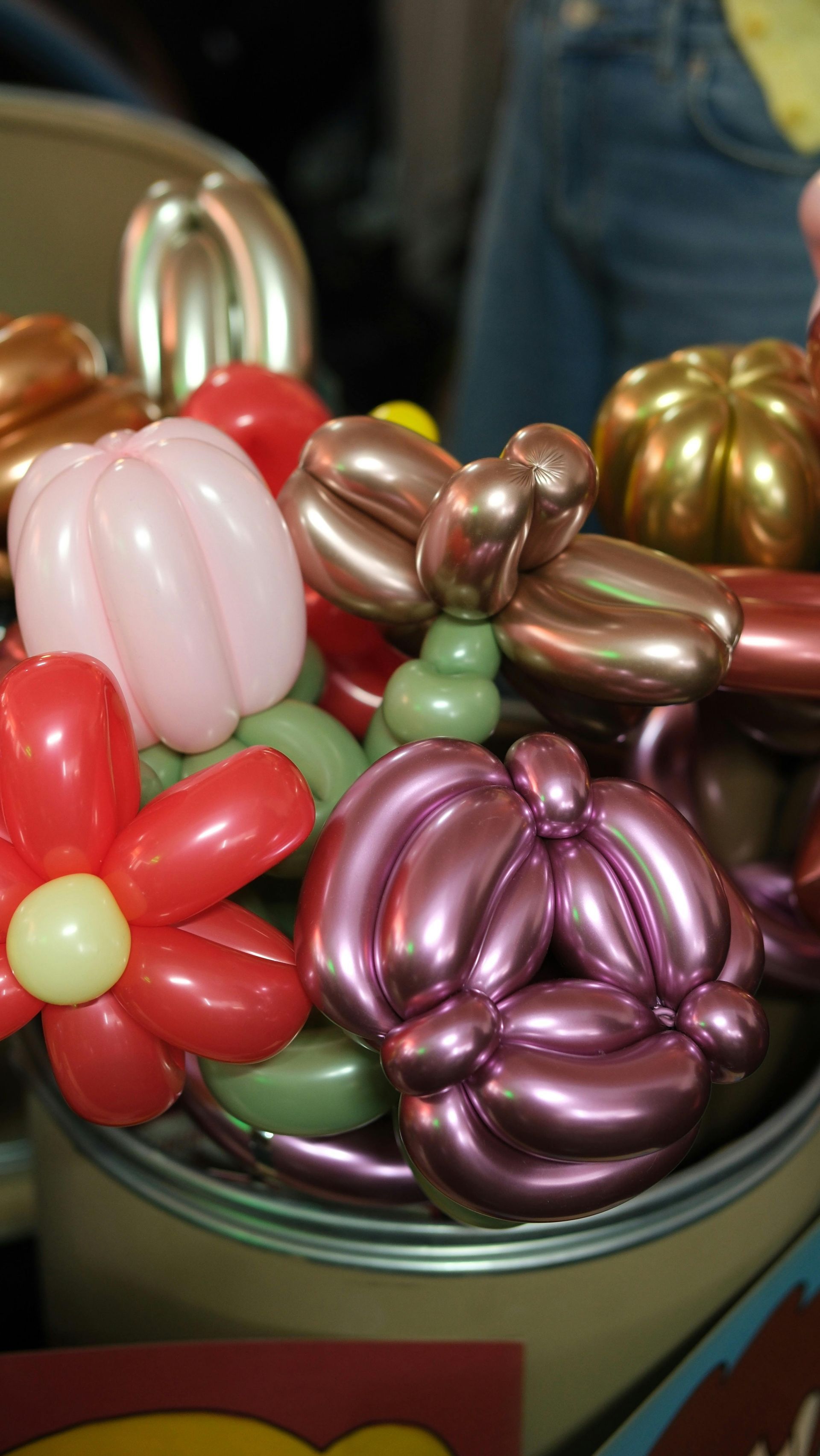 A close-up of a container filled with various colorful balloon sculptures, including flowers and rounded shapes.