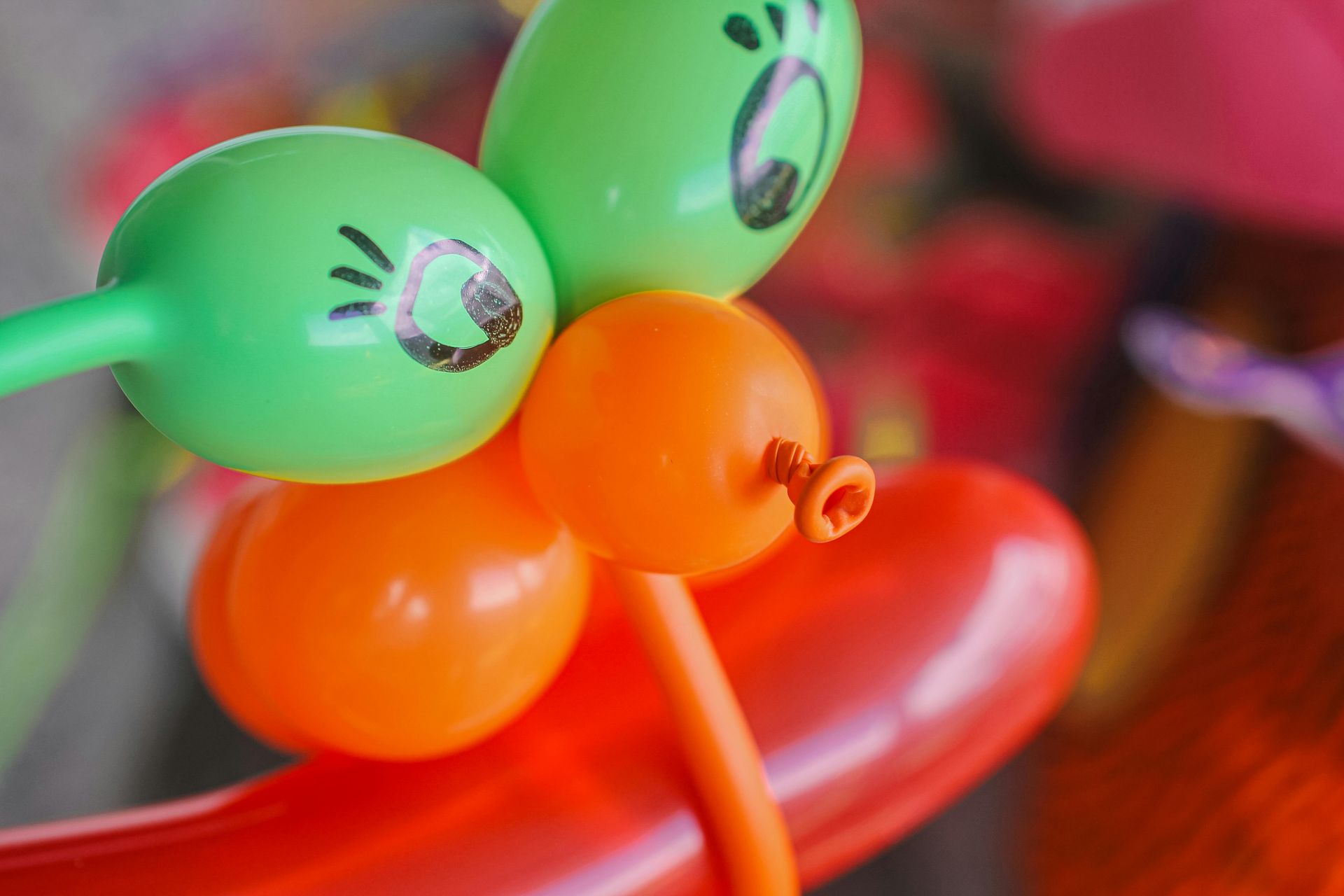 A colorful balloon sculpture featuring two green balloons with drawn eyes, orange balloons, and a large red base.