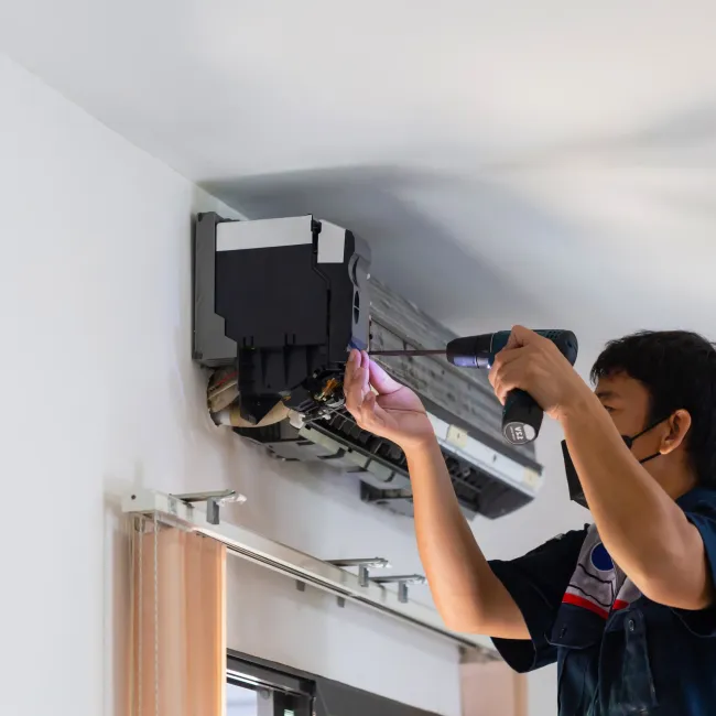 Comfort Air Solution LLC - A man is fixing an air conditioner with a screwdriver.