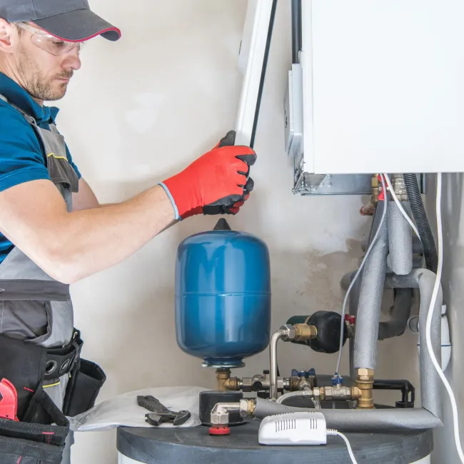 Comfort Air Solution LLC - A man is working on a water heater in a room.