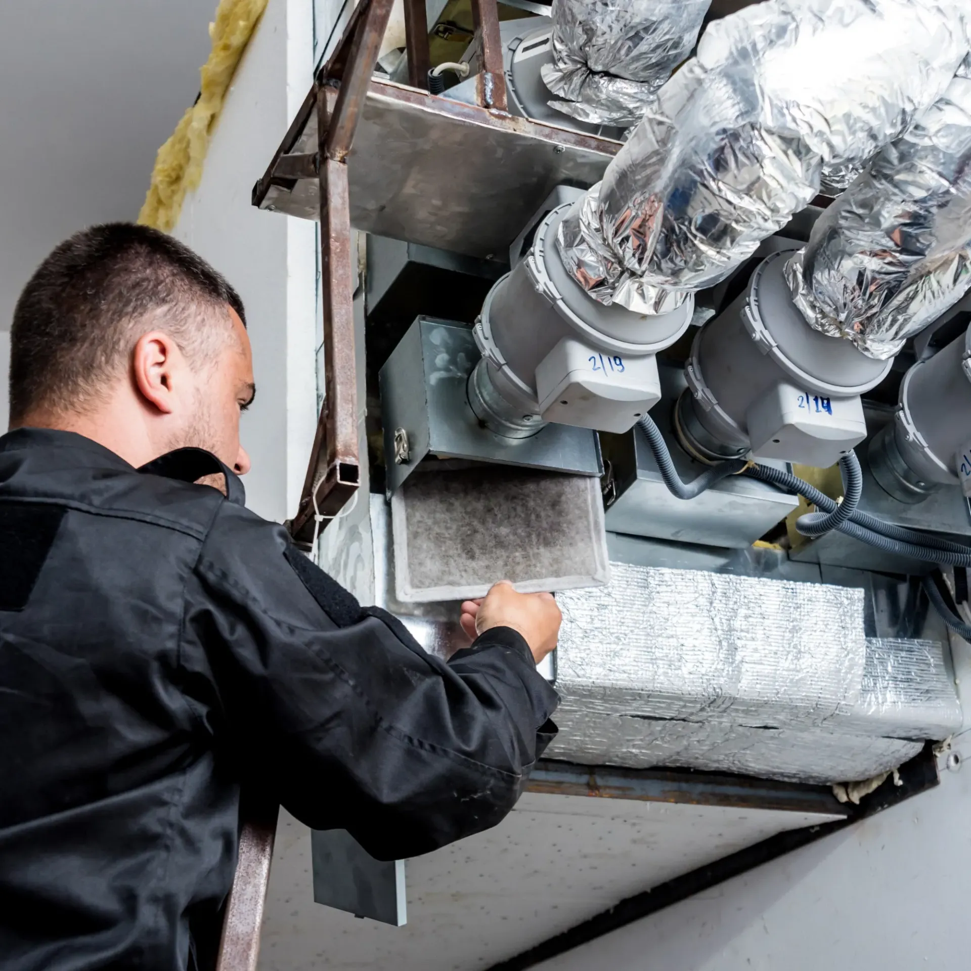 Comfort Air Solution LLC - A man is working on a ventilation system in a building.