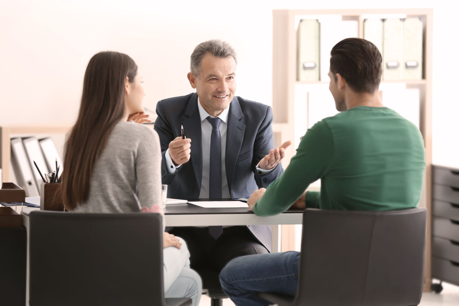 Business meeting with three people seated around a table, discussing with a presenter in a suit