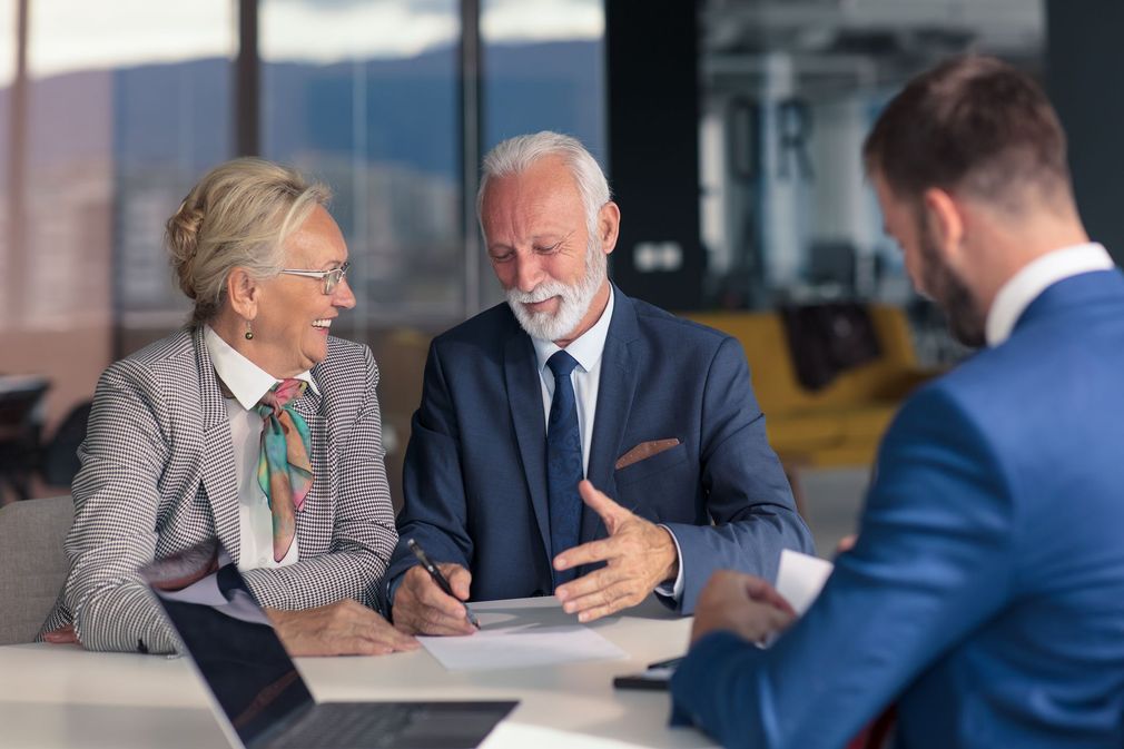 Three businesspeople in a meeting, discussing documents at a conference table.
