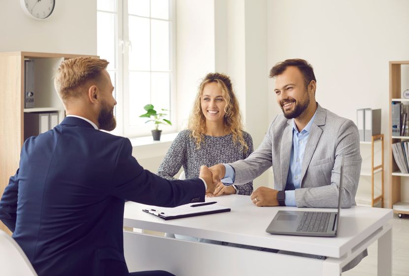 Three coworkers shaking hands at a bright office desk during a meeting