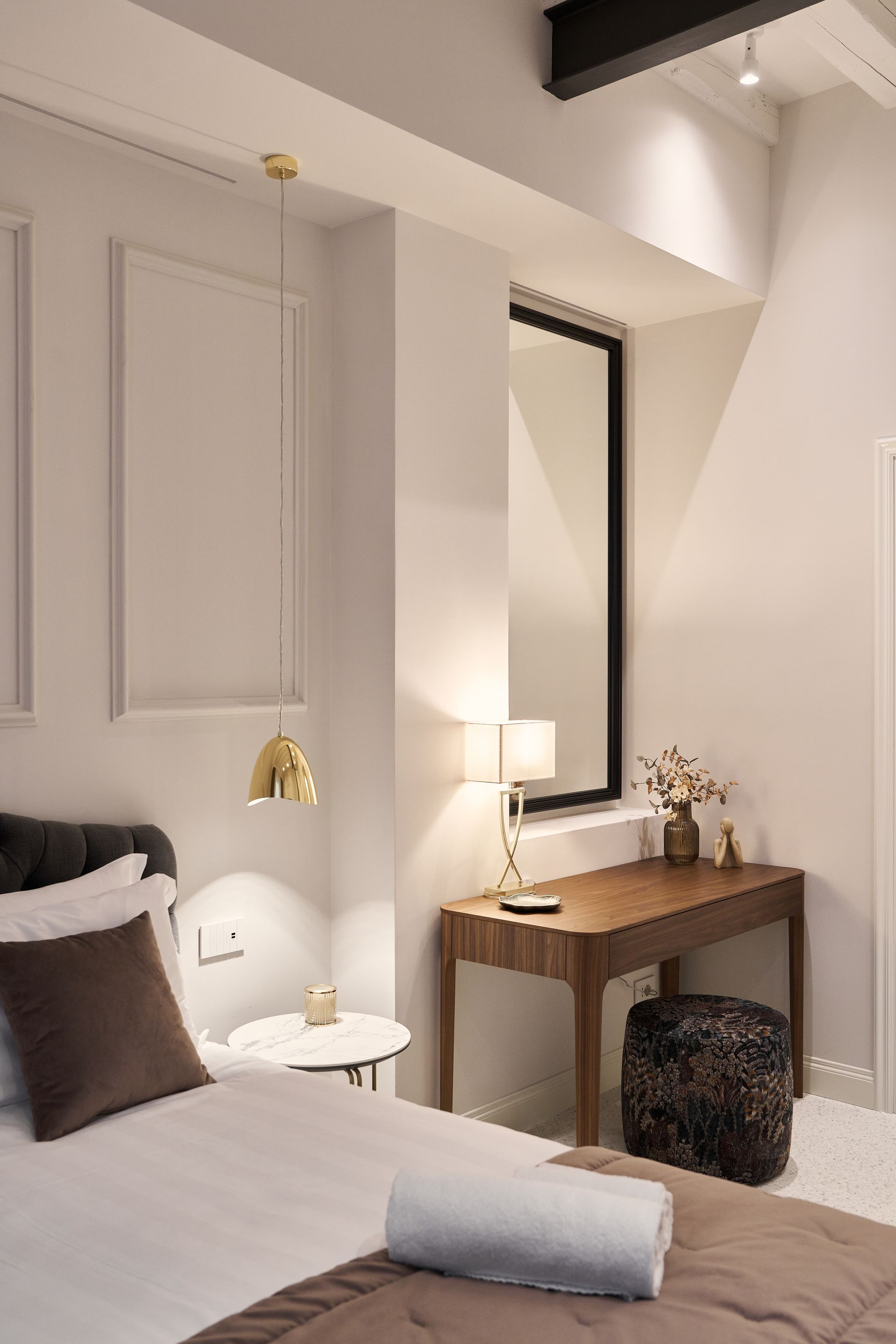 Cozy bedroom with white bed, wooden desk, mirror, lamp, and gold pendant light