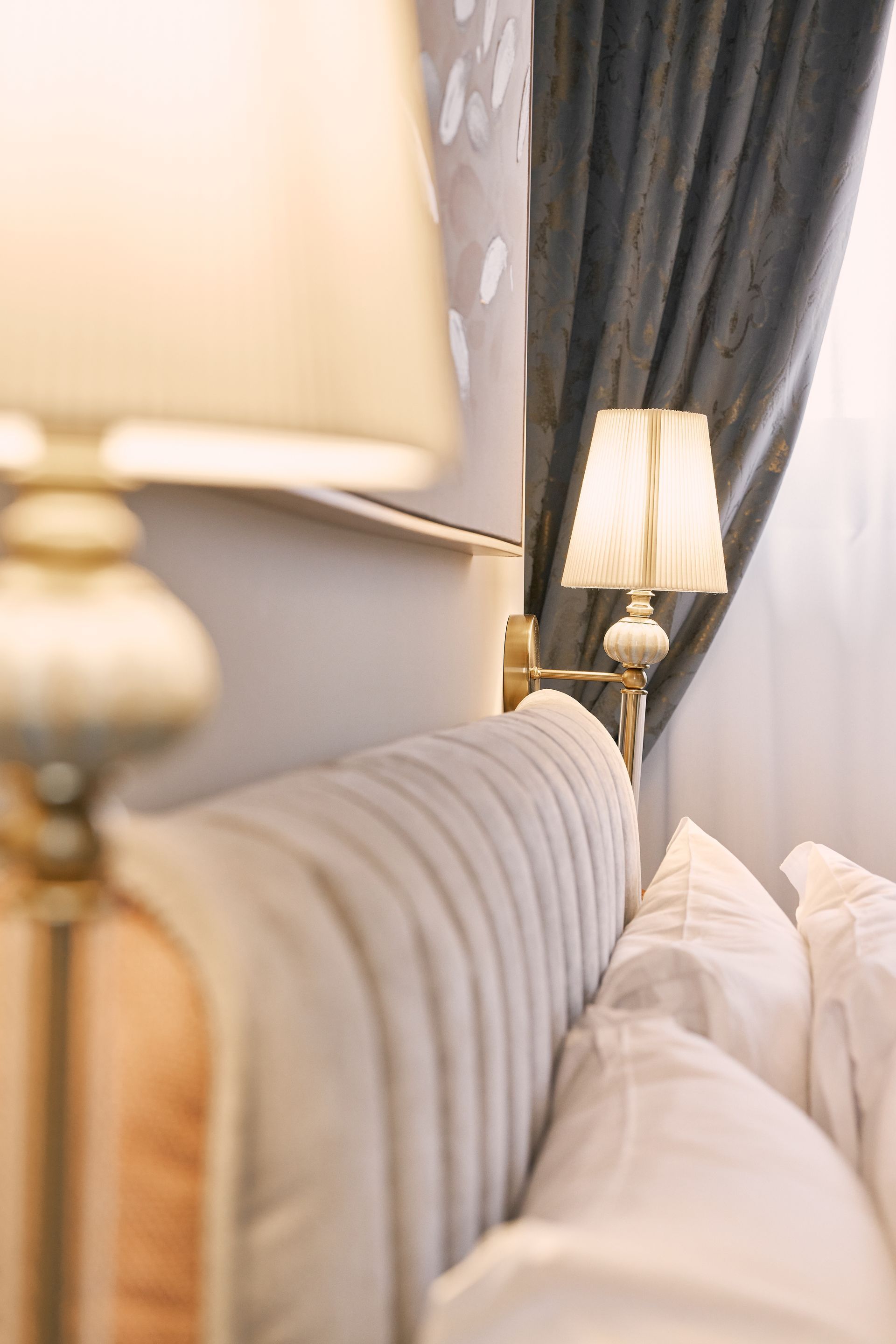 Bedroom with a striped headboard, white pillows, and warm bedside lamps beside dark curtains.