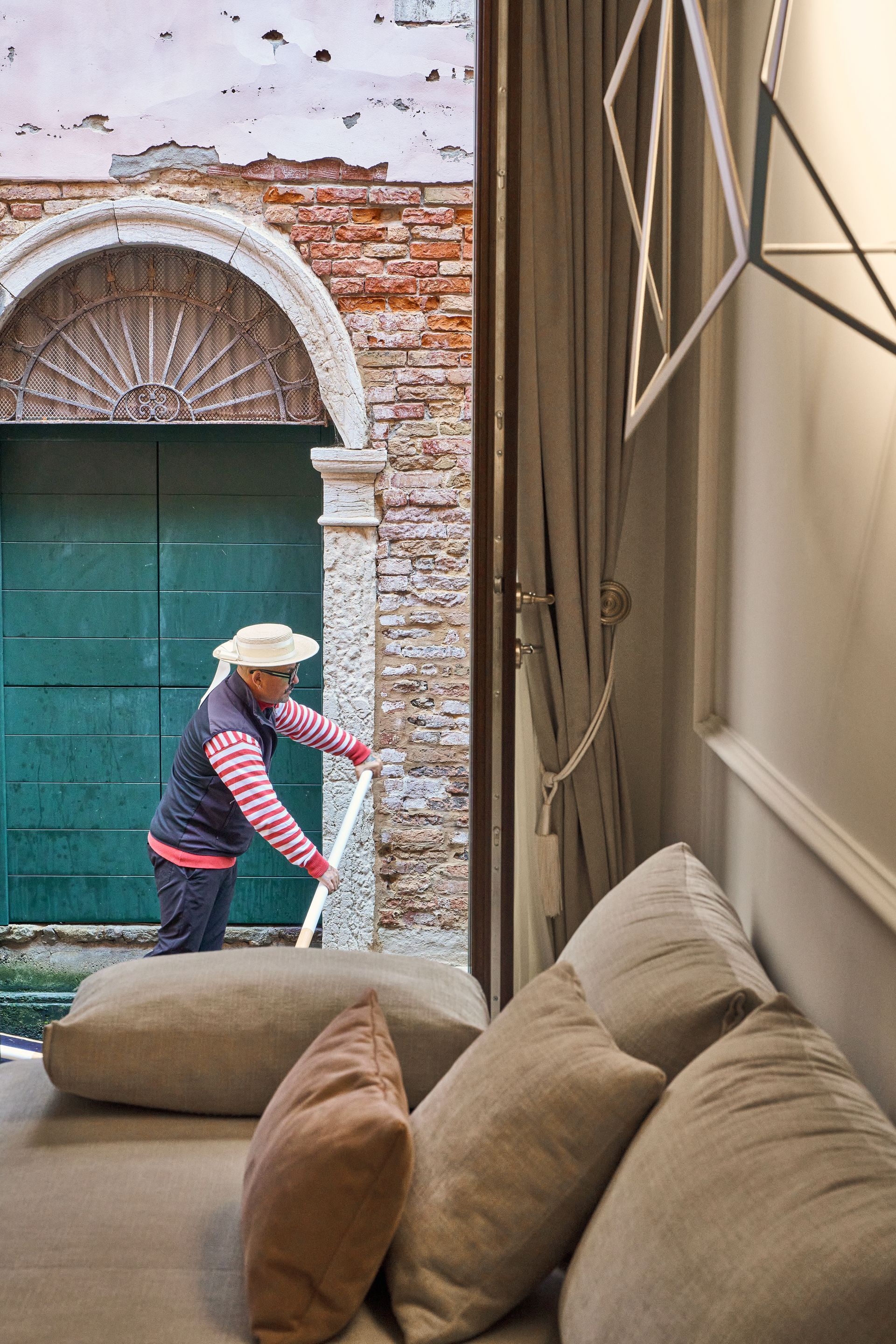 Person sweeping beside a beige sofa in a courtyard with a green door and brick archway