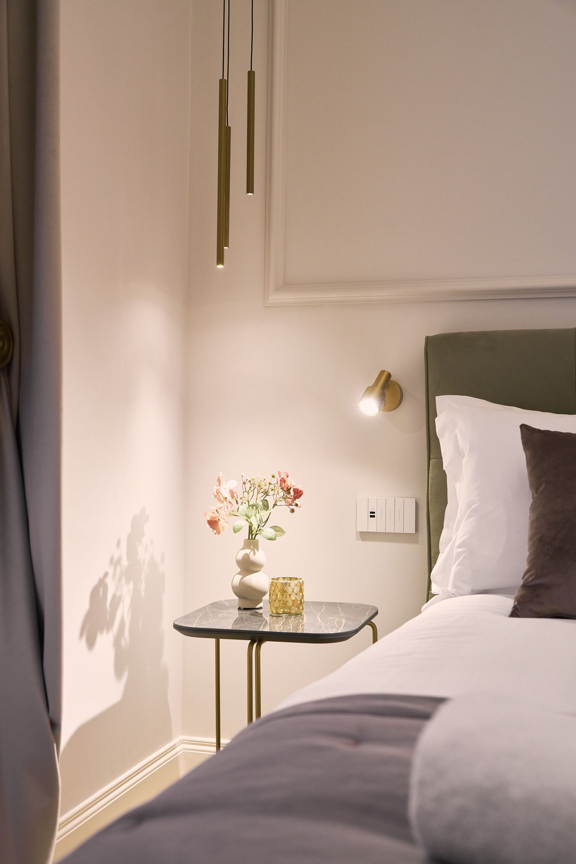 Cozy bedroom corner with a bed, bedside table, flowers, lamp, and soft neutral decor