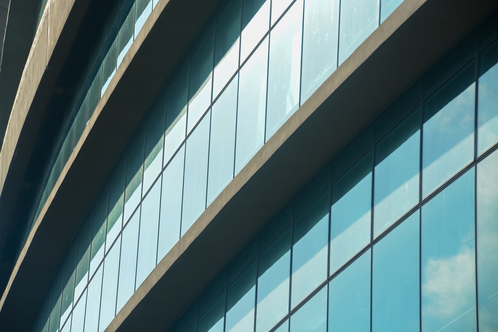 Façade d'un bâtiment moderne avec des rangées de fenêtres en verre reflétant le ciel bleu et les nuages, lignes horizontales.