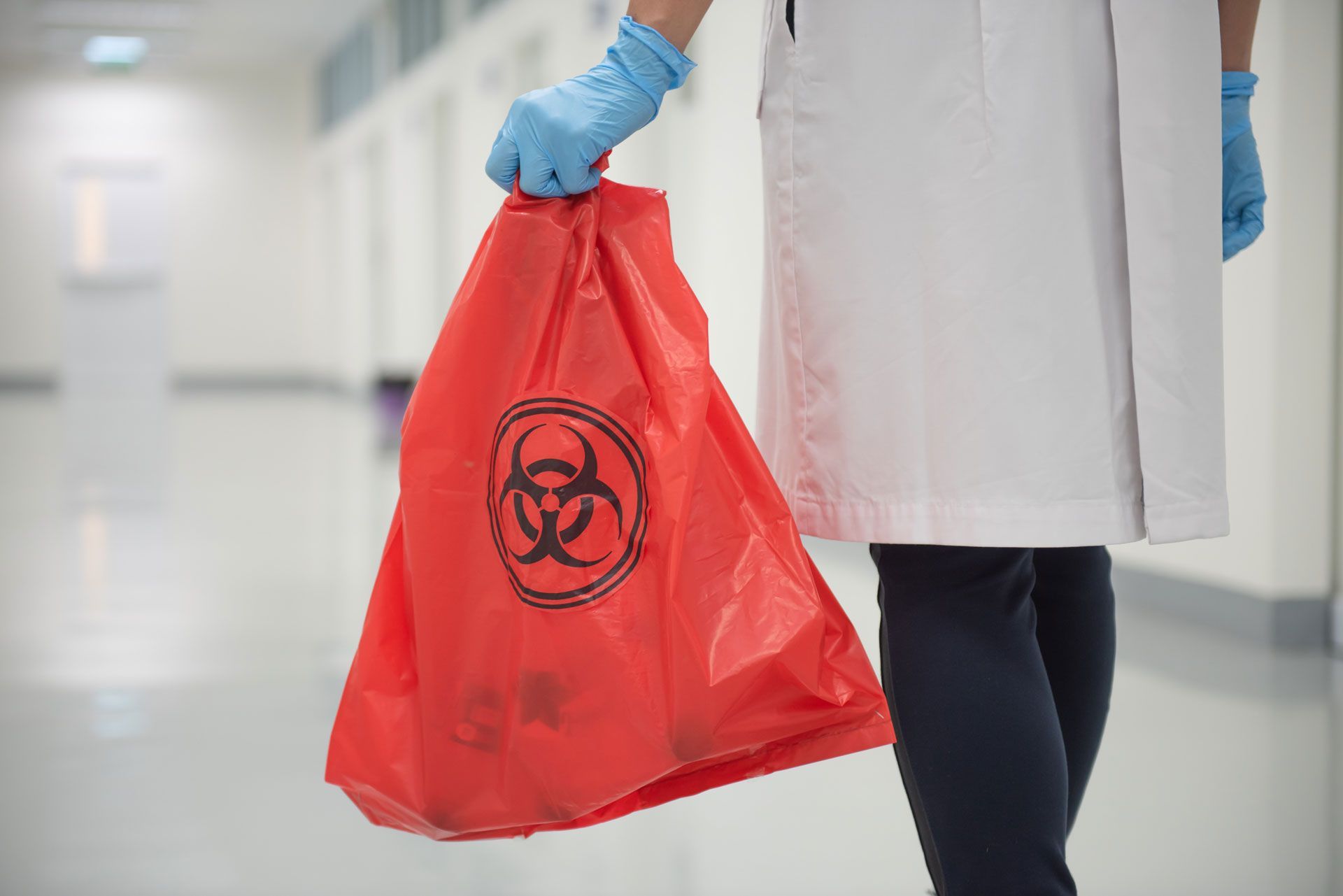 Person holding a red biohazard bag in a hospital hallway.