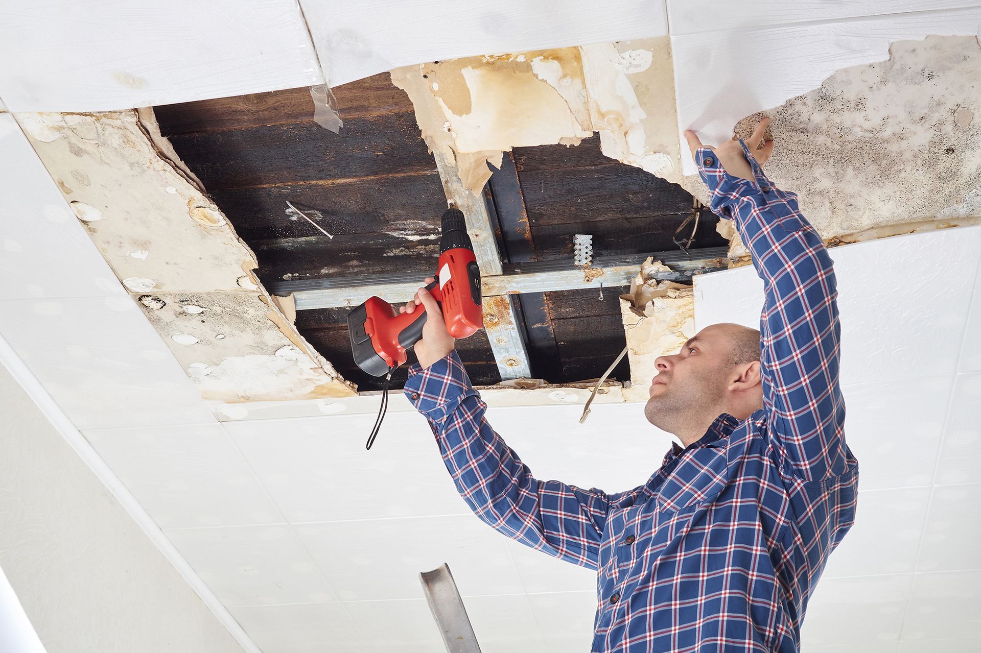 A man is working on a ceiling with a drill.