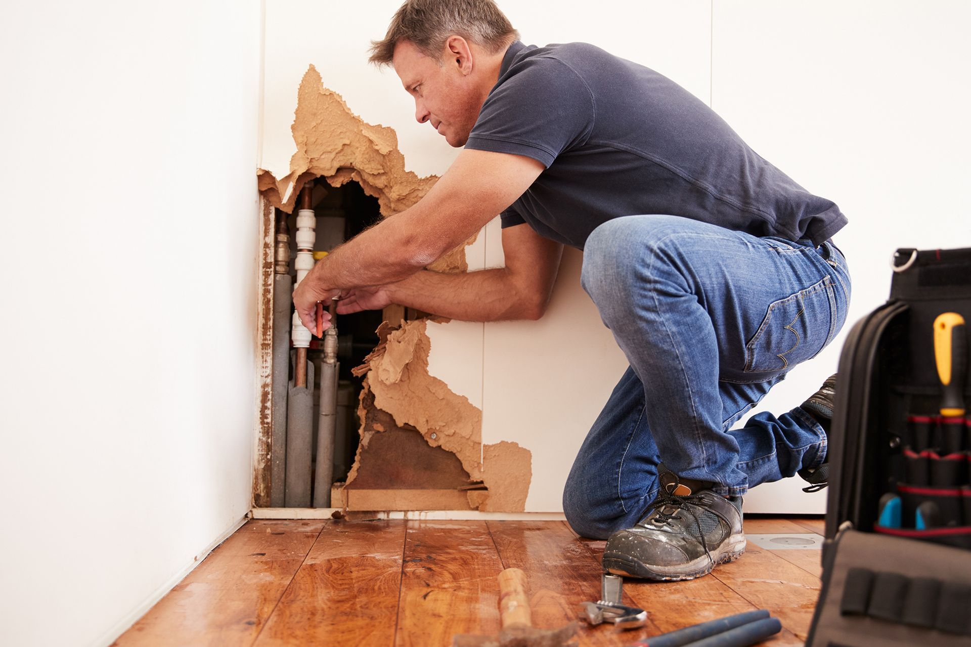 A man is kneeling down in a room fixing a pipe.