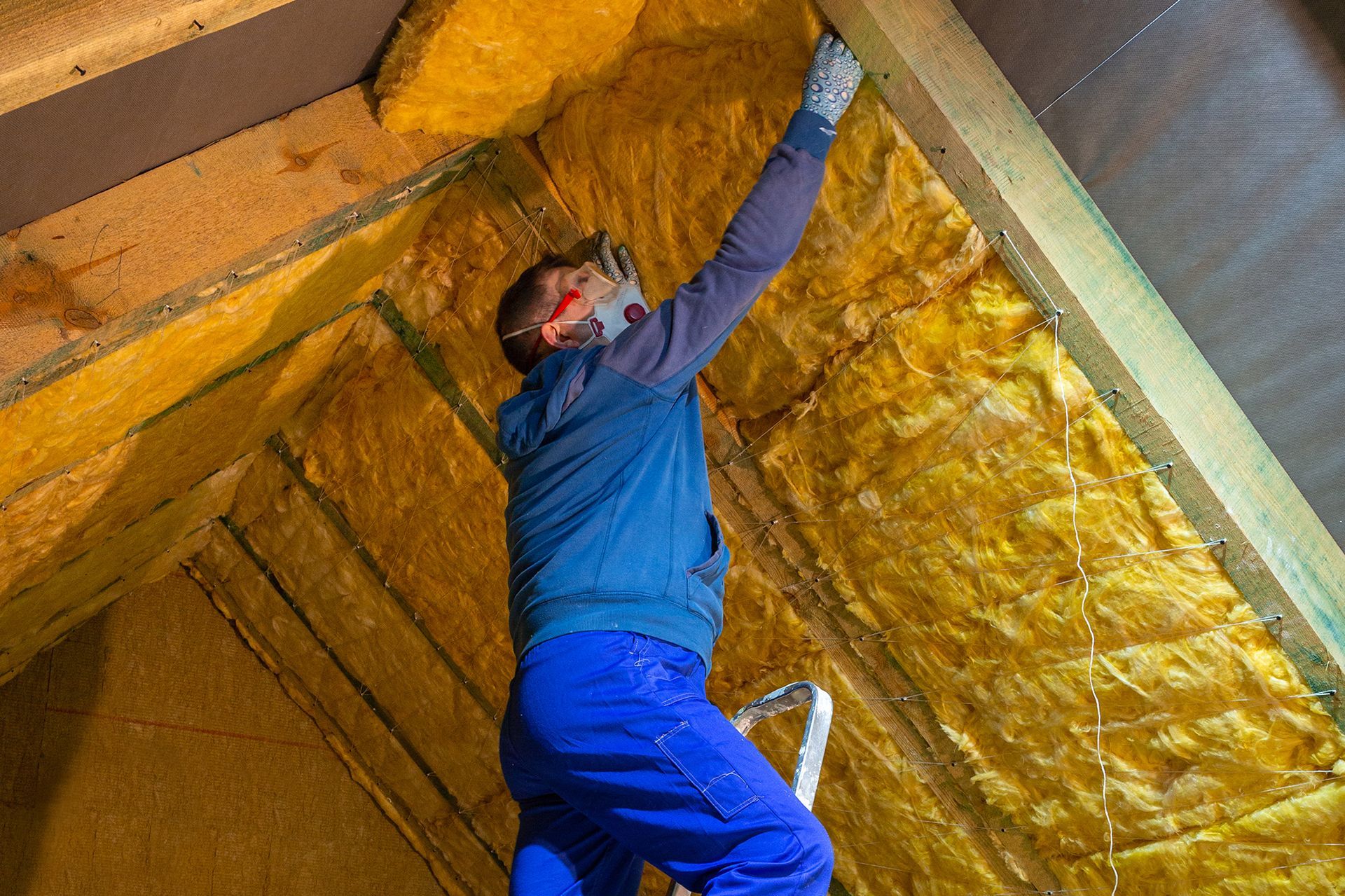 A man is standing on a ladder in an attic.