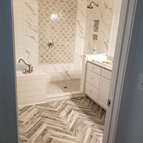 Bright bathroom with herringbone tile floor, glass shower, white vanity, and bathtub.