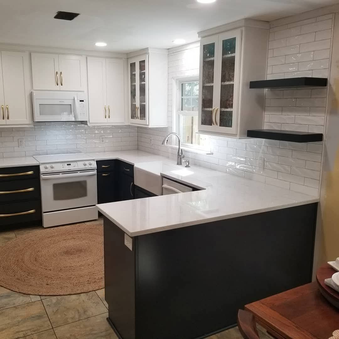 Bright white kitchen with black island, white stove, wood floor, and floating shelves