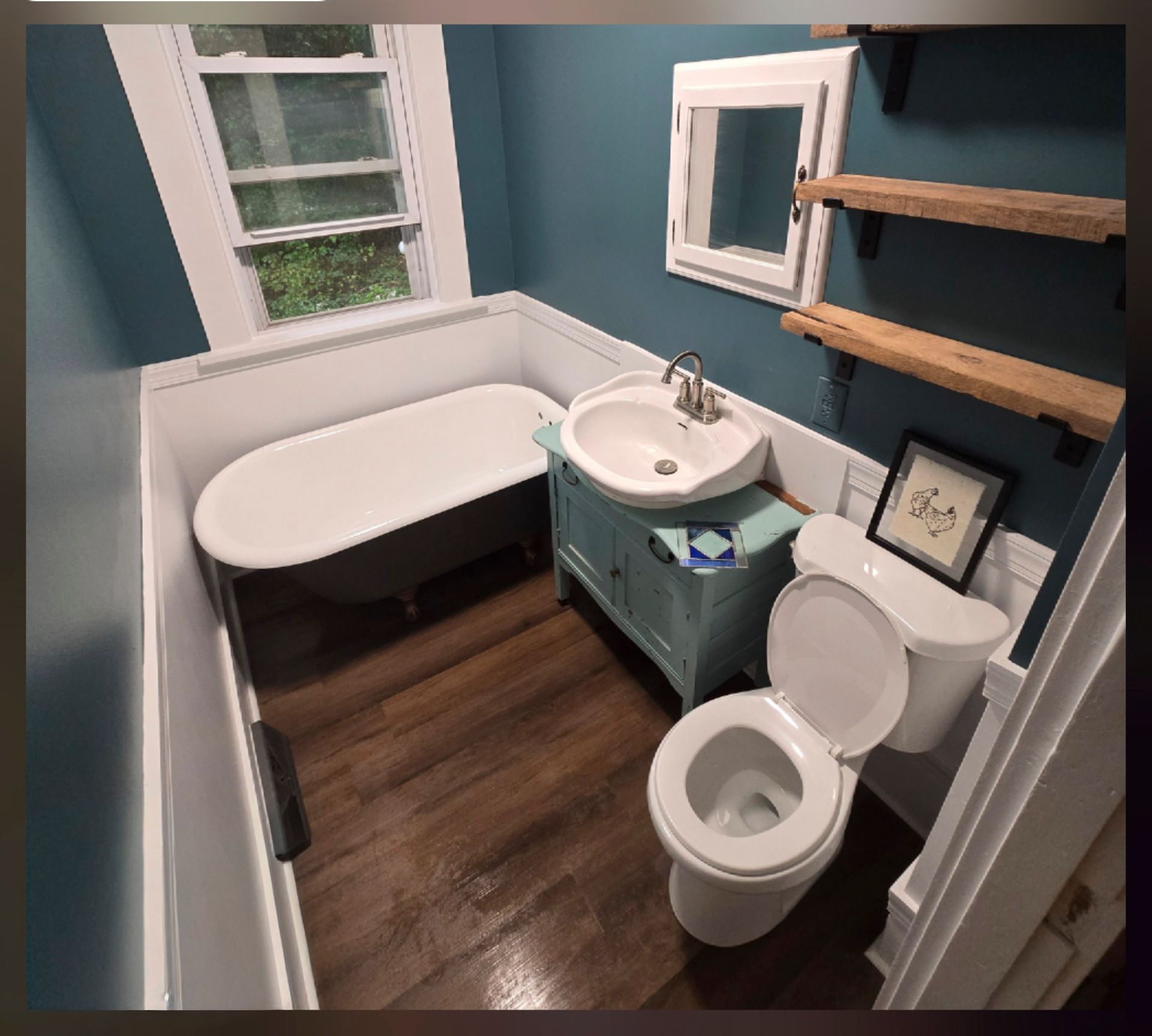 Small bathroom with white clawfoot tub, sink, toilet, teal walls, and dark wood floor.