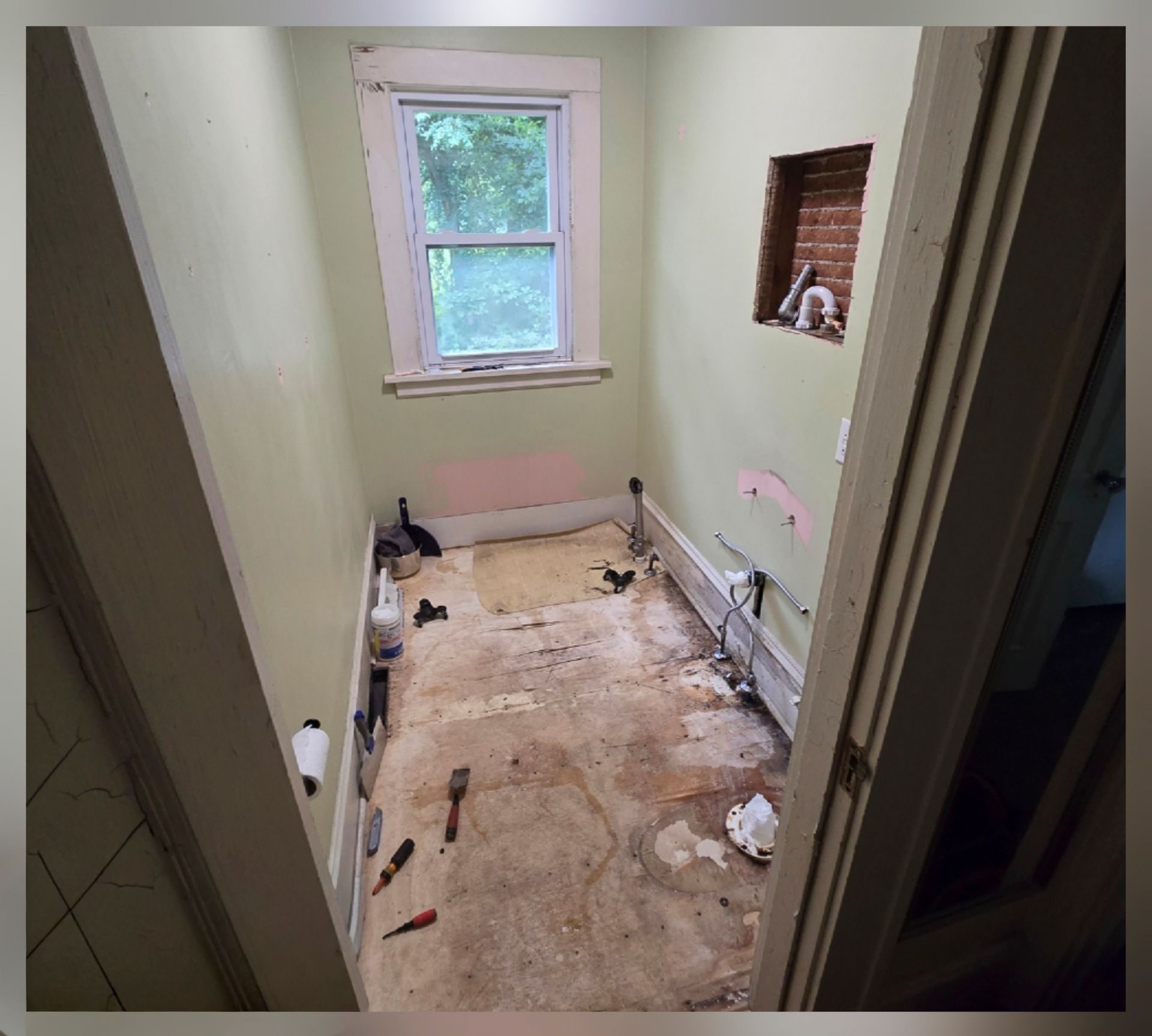 Small unfinished room with bare floor, white walls, window, and exposed brick niche.