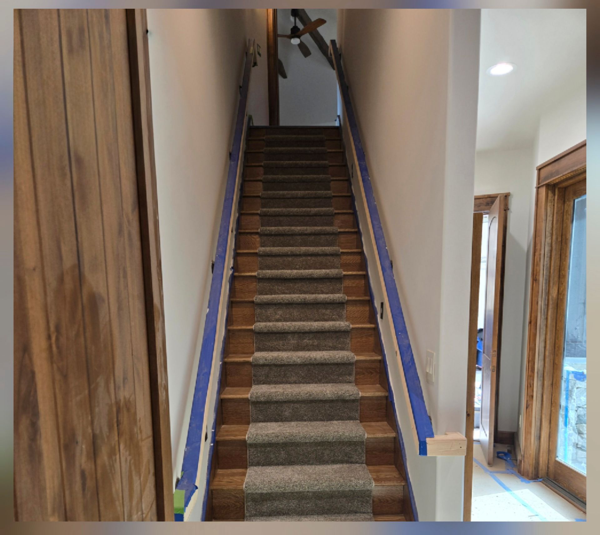 Narrow indoor staircase with carpet runner and wooden trim between hallway walls