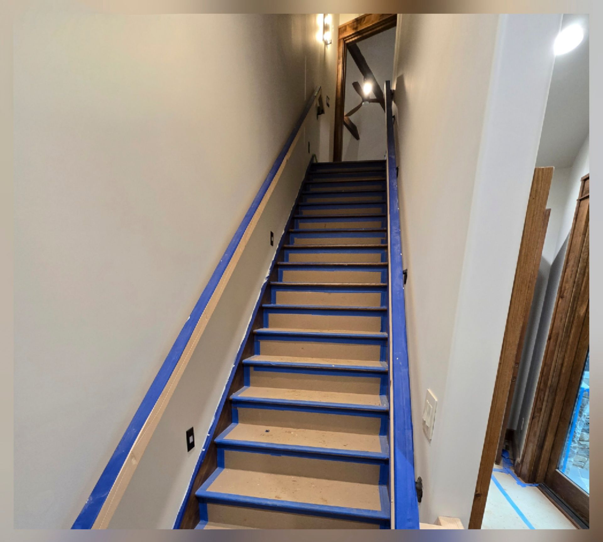 Narrow indoor staircase under construction, with blue-edged steps and white walls.