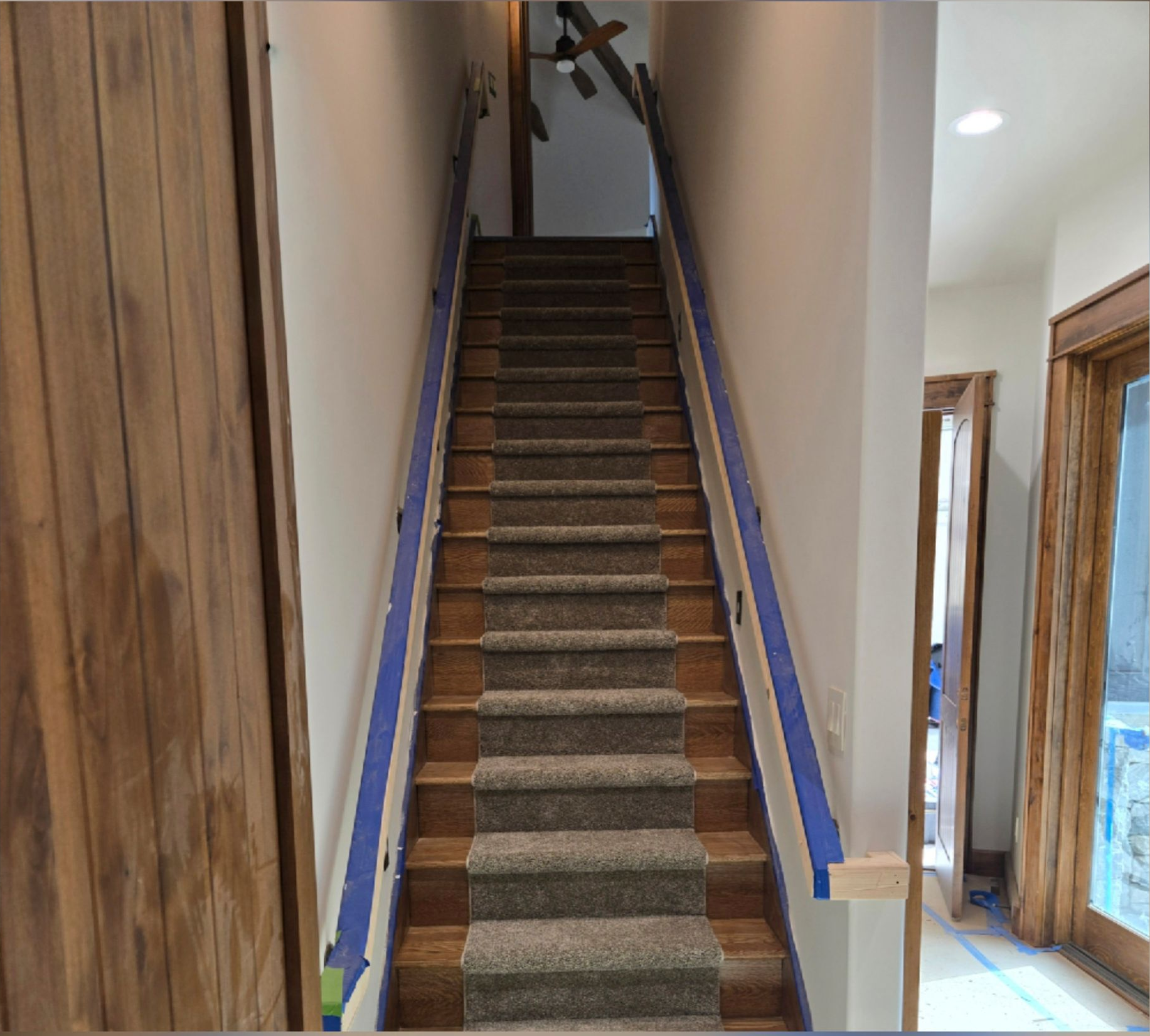 Narrow carpeted staircase in a hallway, with white walls and wood trim, leading upward.