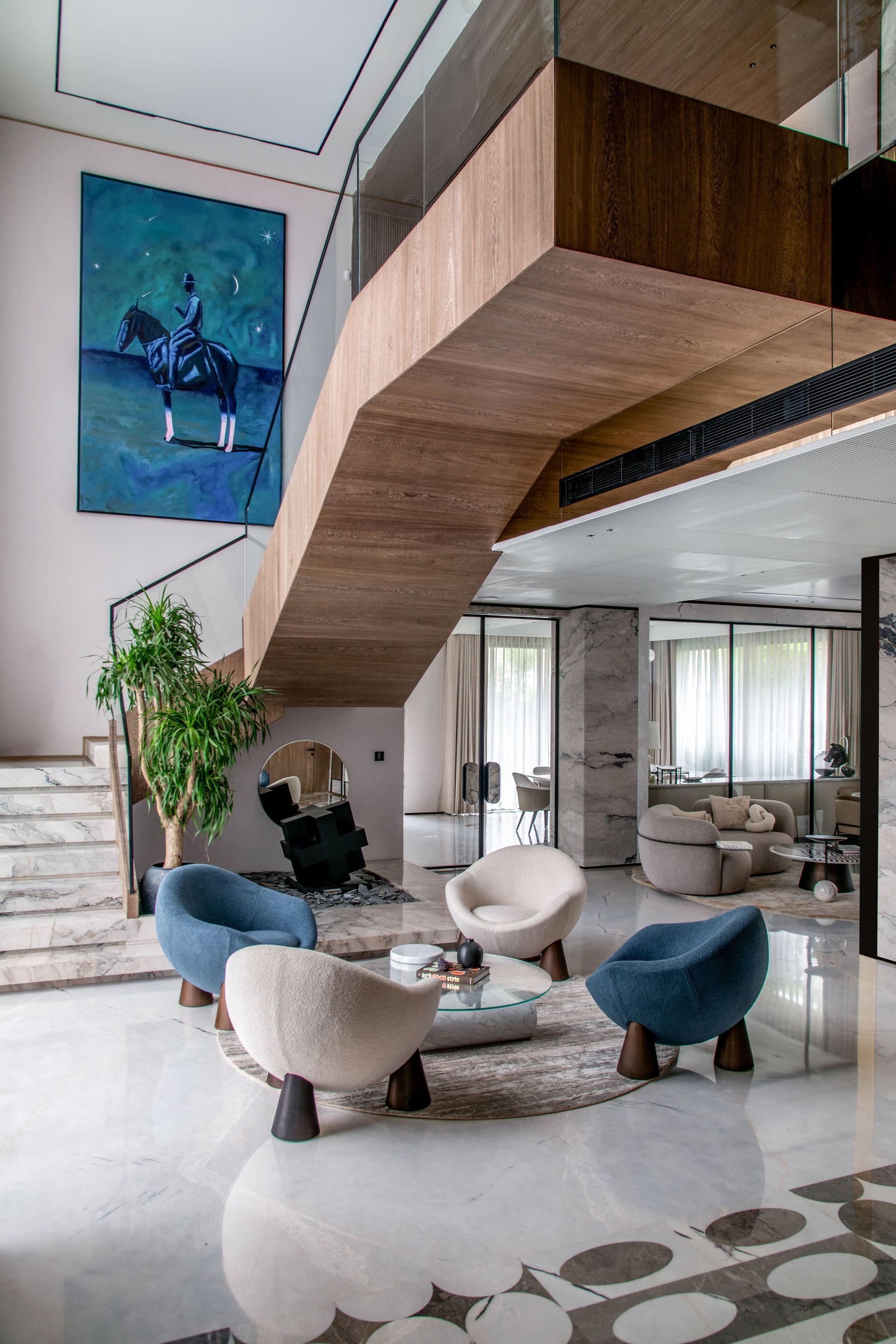 Modern living room with a floating wooden staircase, blue chairs, and a round coffee table