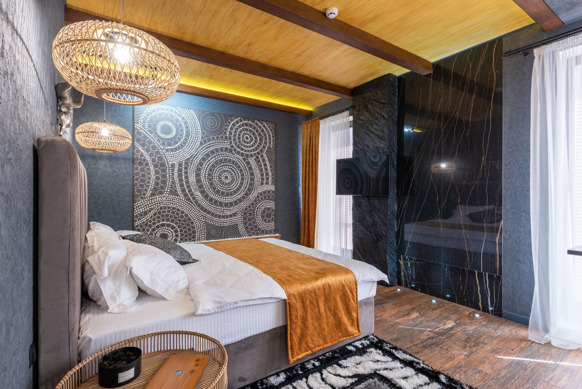 Stylish bedroom with a bed, patterned accent wall, wicker lamps, and a rain view through sheer curtains