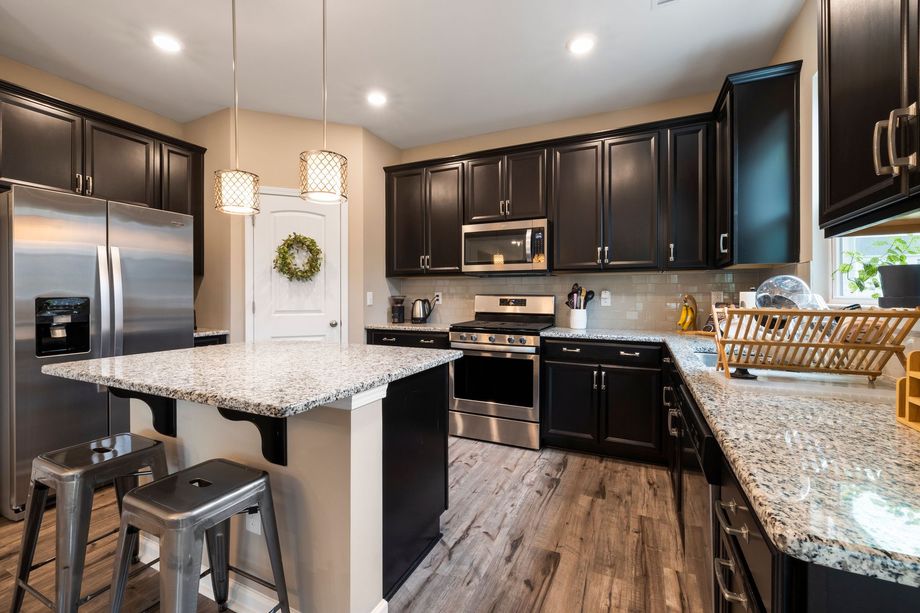 Modern kitchen with dark cabinets, granite island, stainless steel appliances, and gray wood flooring
