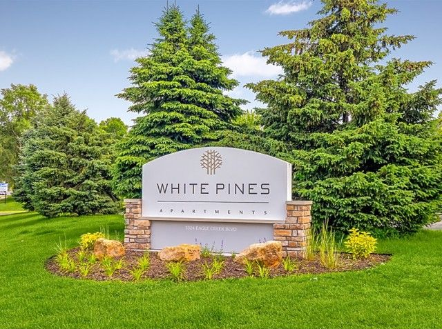 Exterior sign for White Pines Apartments with a landscaped lawn and trees.